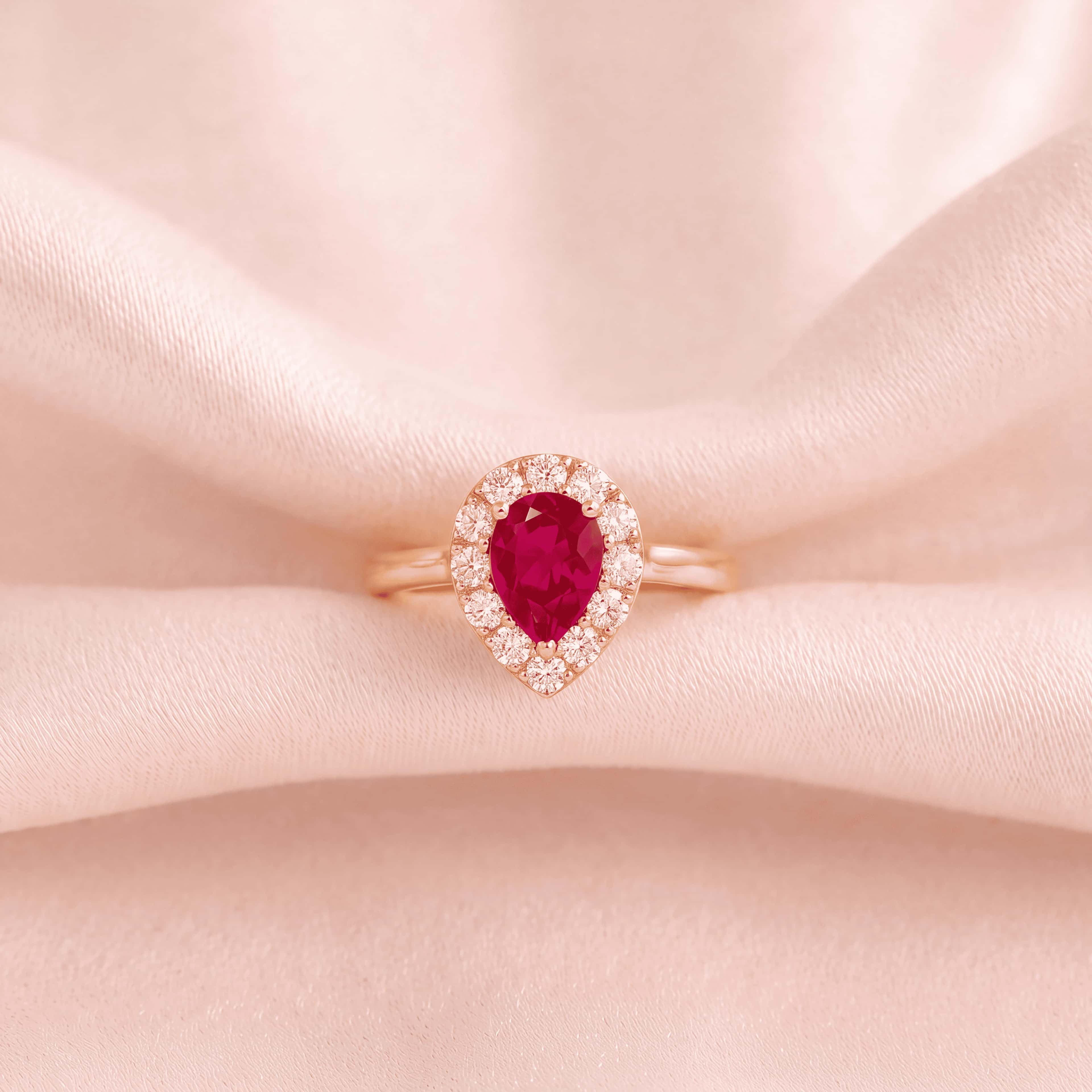 Pear-cut ruby halo ring in rose gold on pink silk
