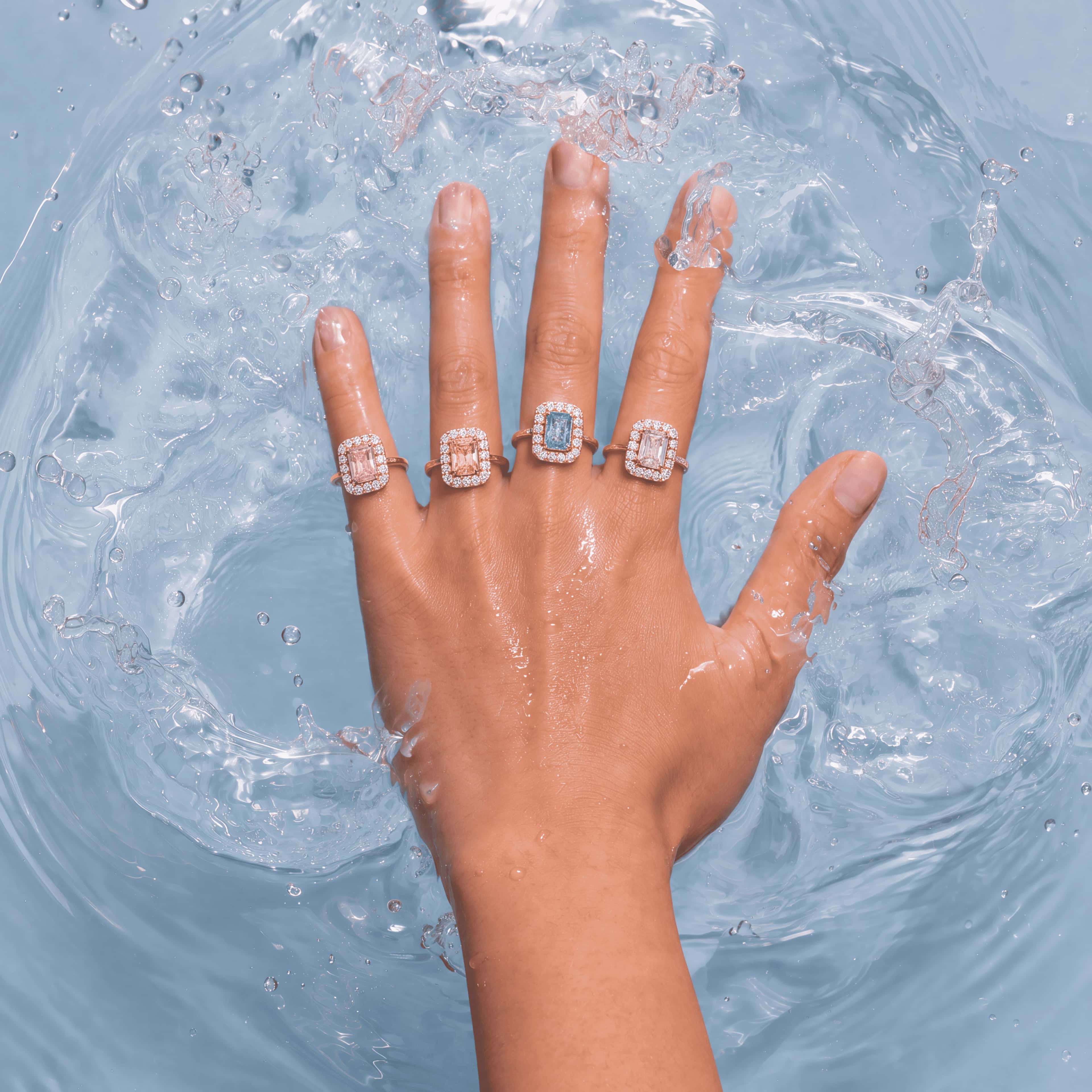 Coloured gemstone halo rings worn on a hand resting in water